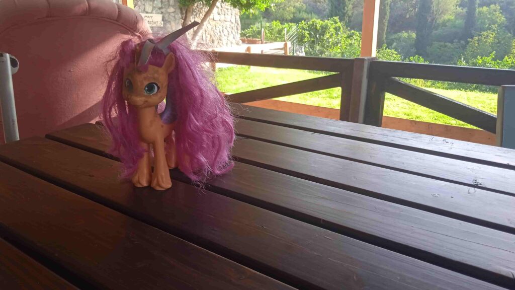 „Spielzeug-Einhorn mit rosa Mähne und großen blauen Augen auf Holztisch – symbolisches Bild für die Geschichte ‚Chatty und das Stöckchen‘.“