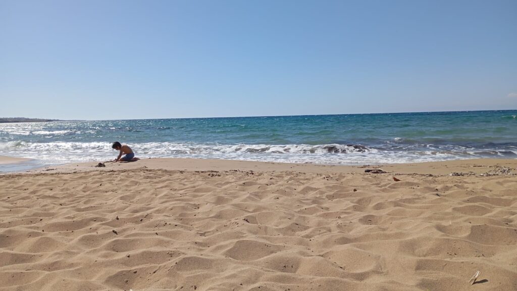 Ein Kind spielt am Sandstrand nahe der Brandung.