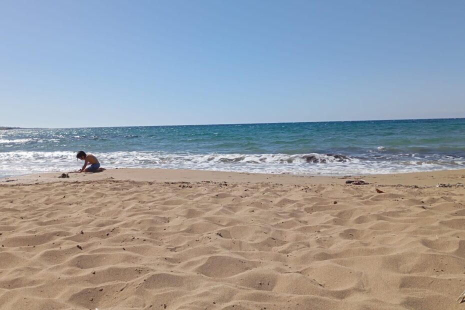 Ein Kind spielt am Sandstrand nahe der Brandung.