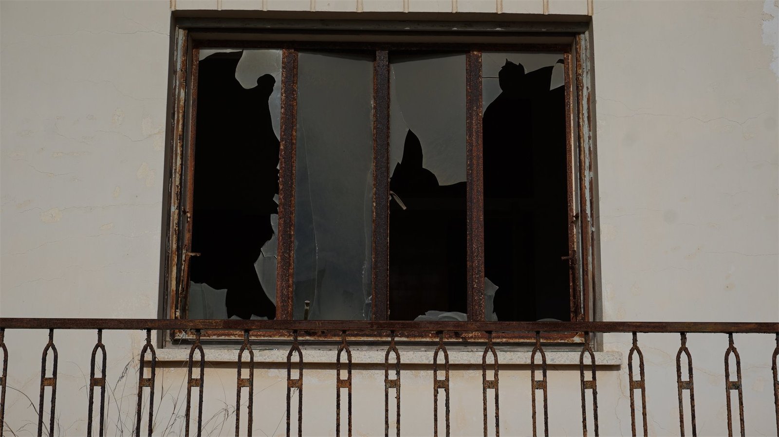 Zerbrochenes Fenster hinter rostigen Gittern in einer verlassenen Hausfassade.